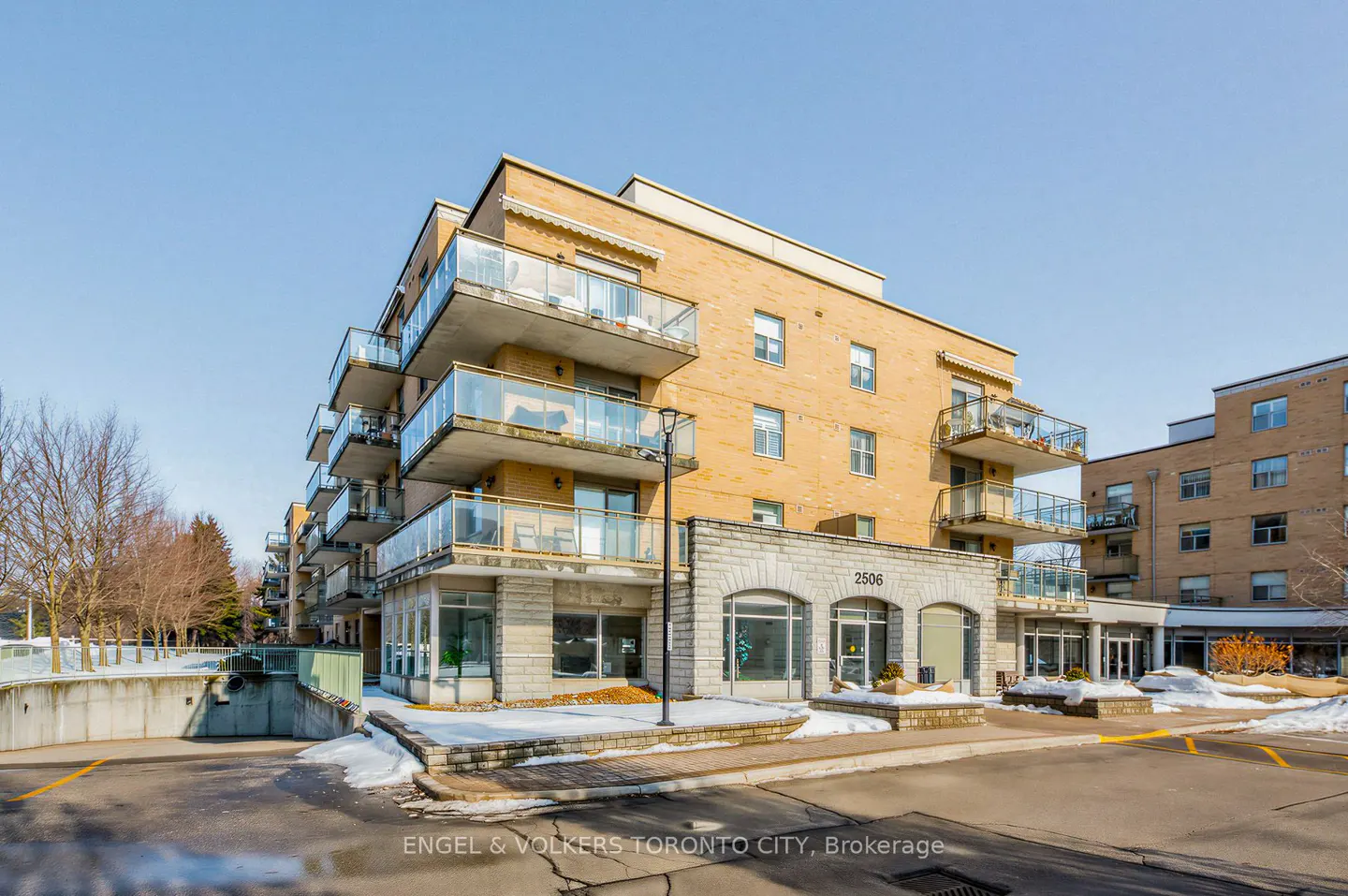 Exterior view of a yellow brick apartment building with glass balconies and a stone facade on a sunny day.
