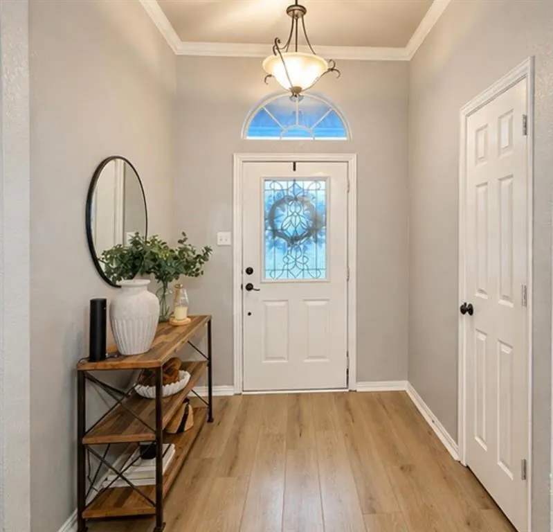 Entryway with light wood floors, gray walls, and white trim. A console table with decor sits to the left of the white front door.
