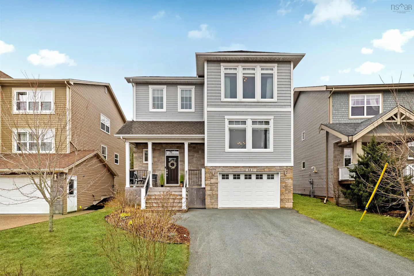 Three-story gray house with white trim, stone accents, and a white garage door. A wreath hangs on the front door.
