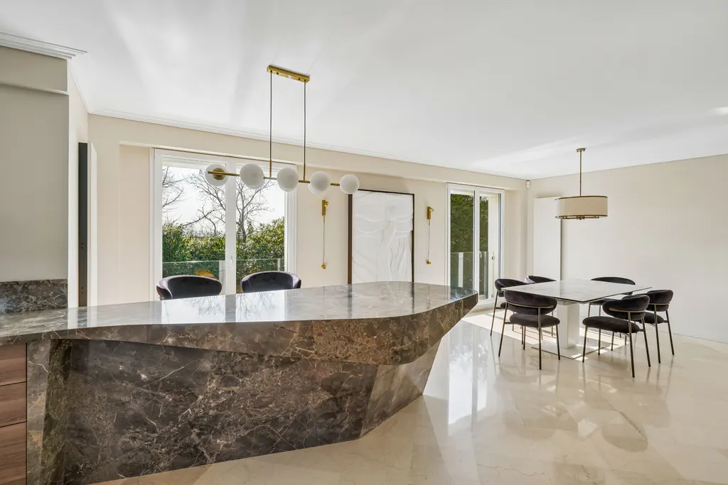 A modern kitchen with a marble island, dining table with black chairs, and large windows.