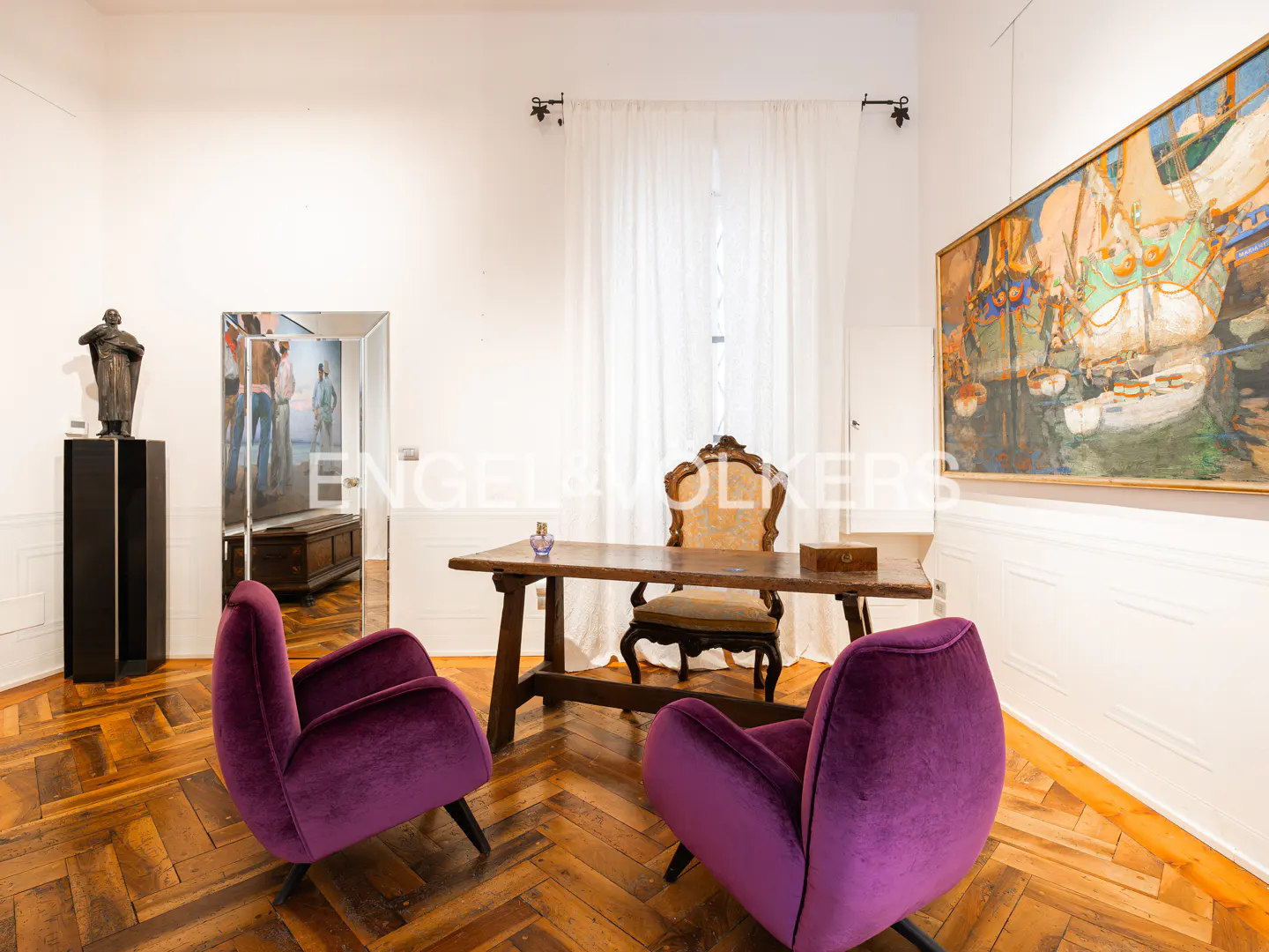 Interior view of a room with purple chairs, a wooden desk, and art on the walls, on a herringbone wood floor.