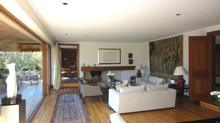Bright living room with hardwood floors, white sofas, and a fireplace. A tapestry hangs on the wall. Glass doors open to a patio.