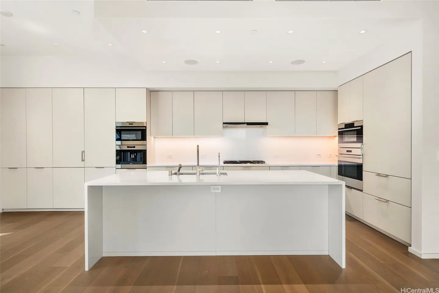 Bright, modern kitchen with white cabinets, island, stainless steel appliances, and wood floors.