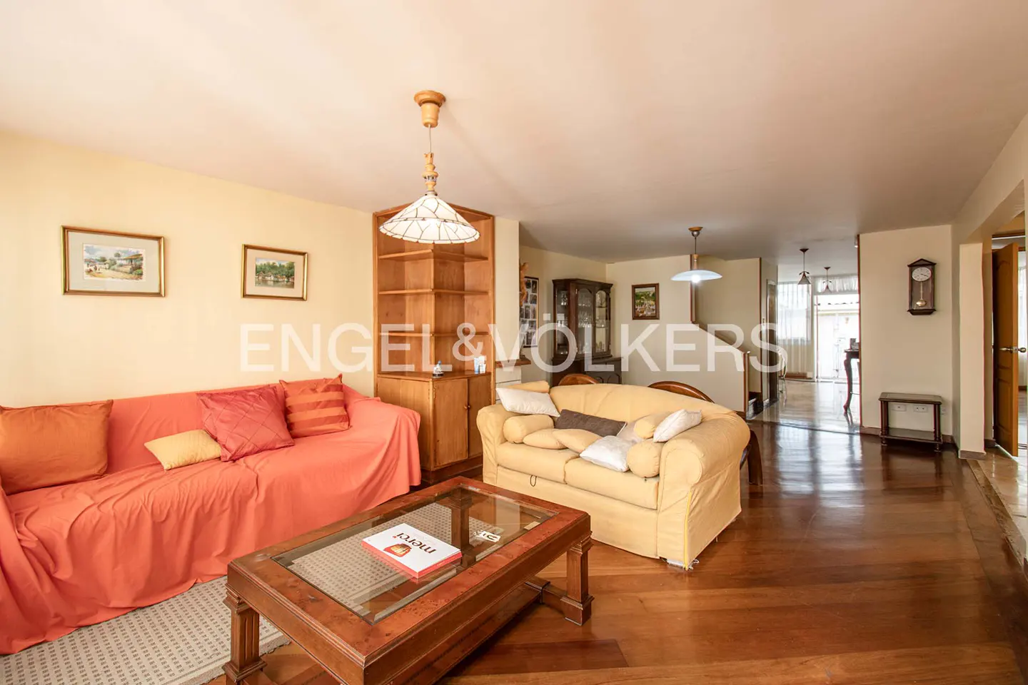 A living room with a coral sofa, yellow sofa, wood floors, and a glass-topped coffee table.