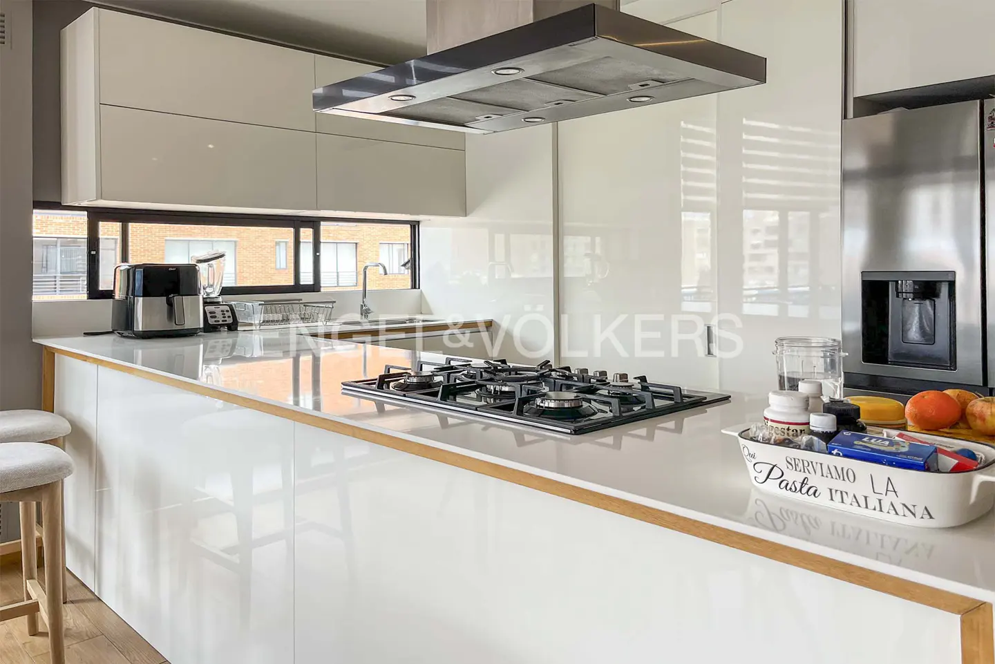Modern kitchen with white cabinets, stainless steel appliances, and a gas cooktop on a white countertop. A window provides natural light.