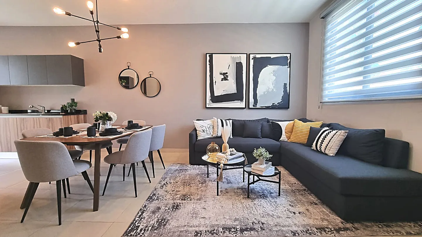 A modern living and dining area with a gray L-shaped sofa, a wooden dining table with gray chairs, and abstract art on the wall.
