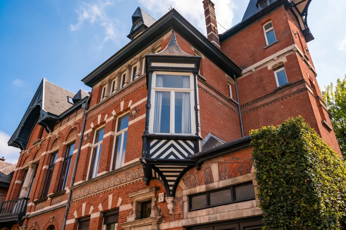 Exterior view of a red brick building with a bay window and black and white chevron detailing.