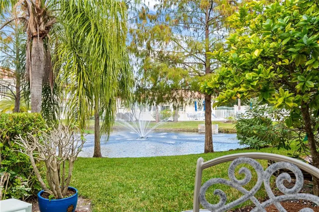 View from patio with green lawn, trees, and pond with fountain. A chair is partially visible in the foreground.