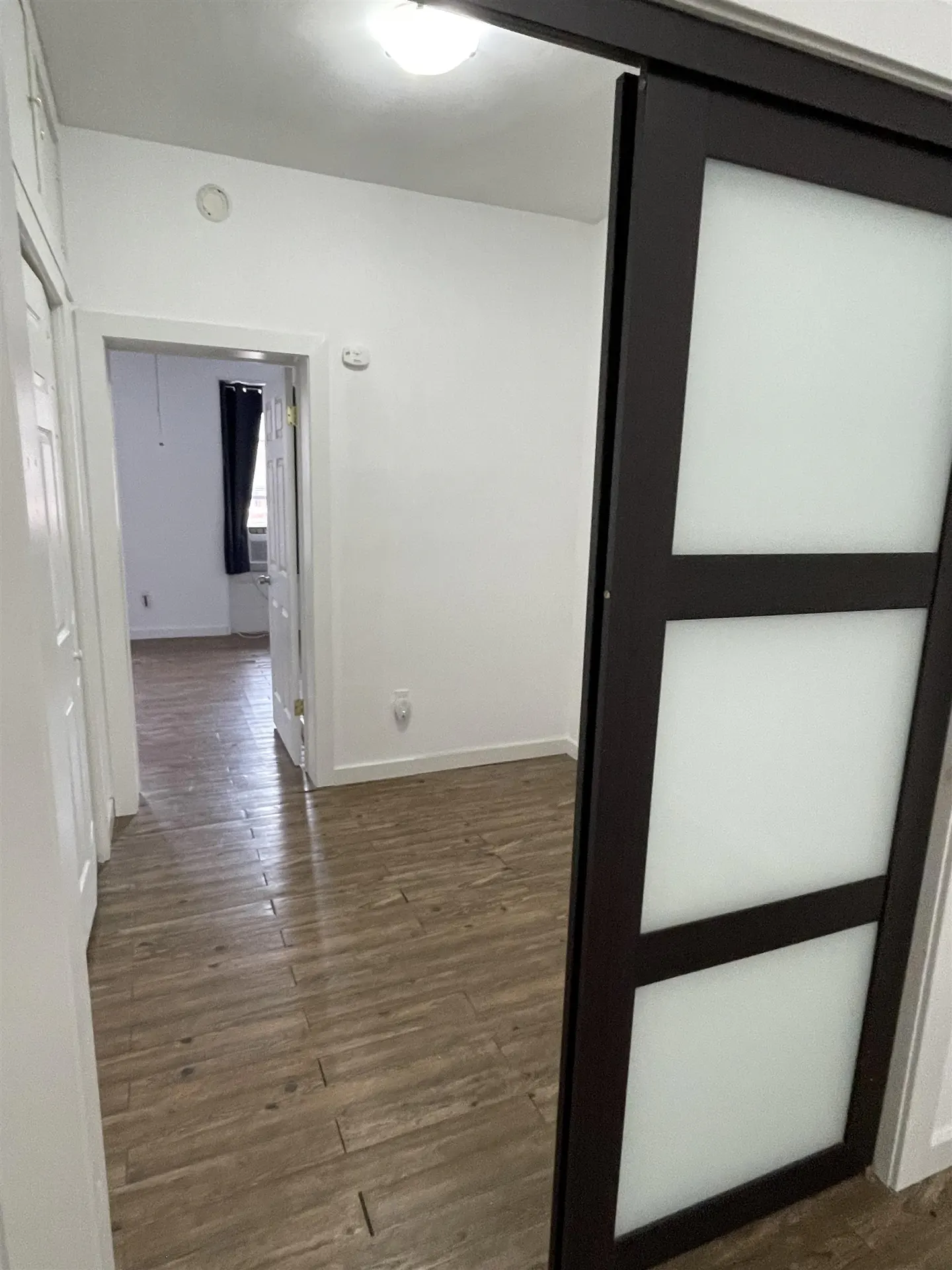 A bright room with wood-look floors, white walls, and a dark brown sliding door with frosted glass panels.