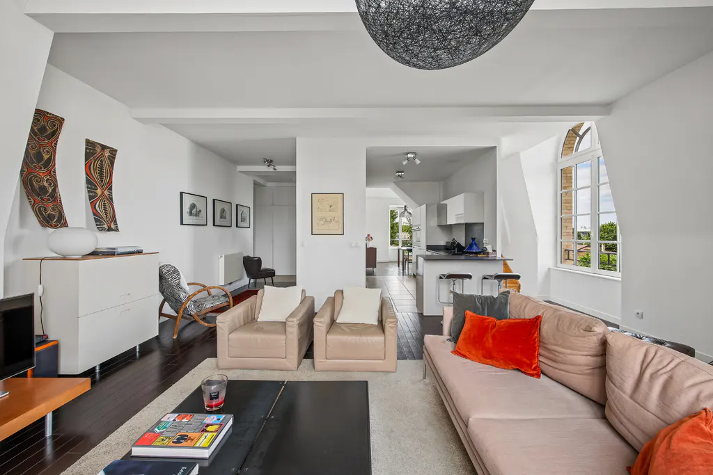 Modern living room with beige sofa, two leather armchairs, black coffee table, and an open kitchen with a breakfast bar.