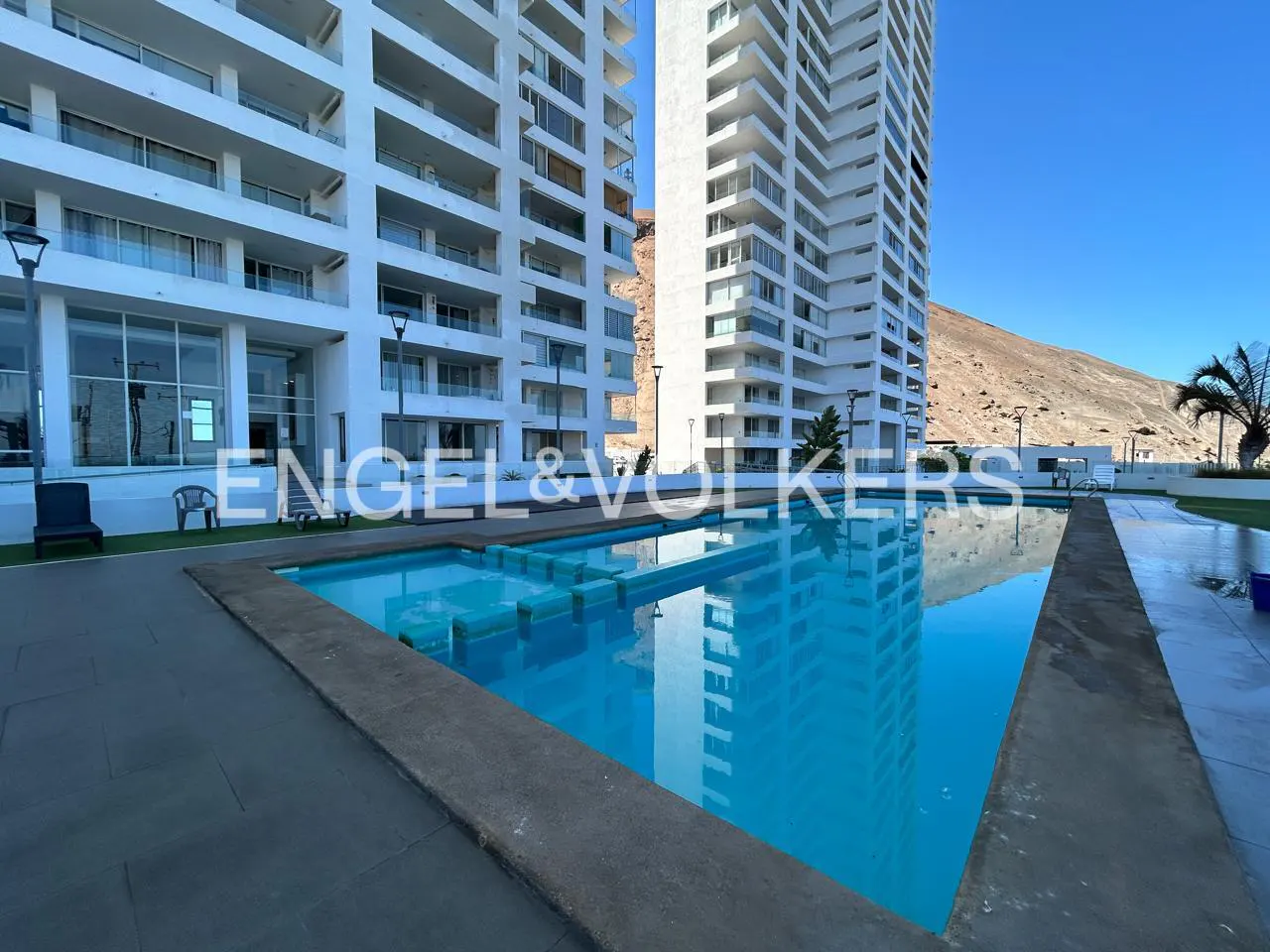 Exterior view of a blue swimming pool in front of two white high-rise apartment buildings.