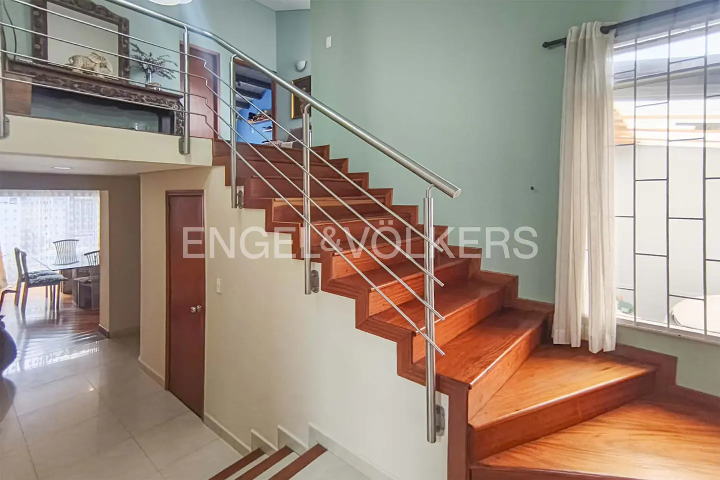 Interior view of a home featuring wooden stairs with stainless steel railings, leading to a second floor with a decorative mirror.