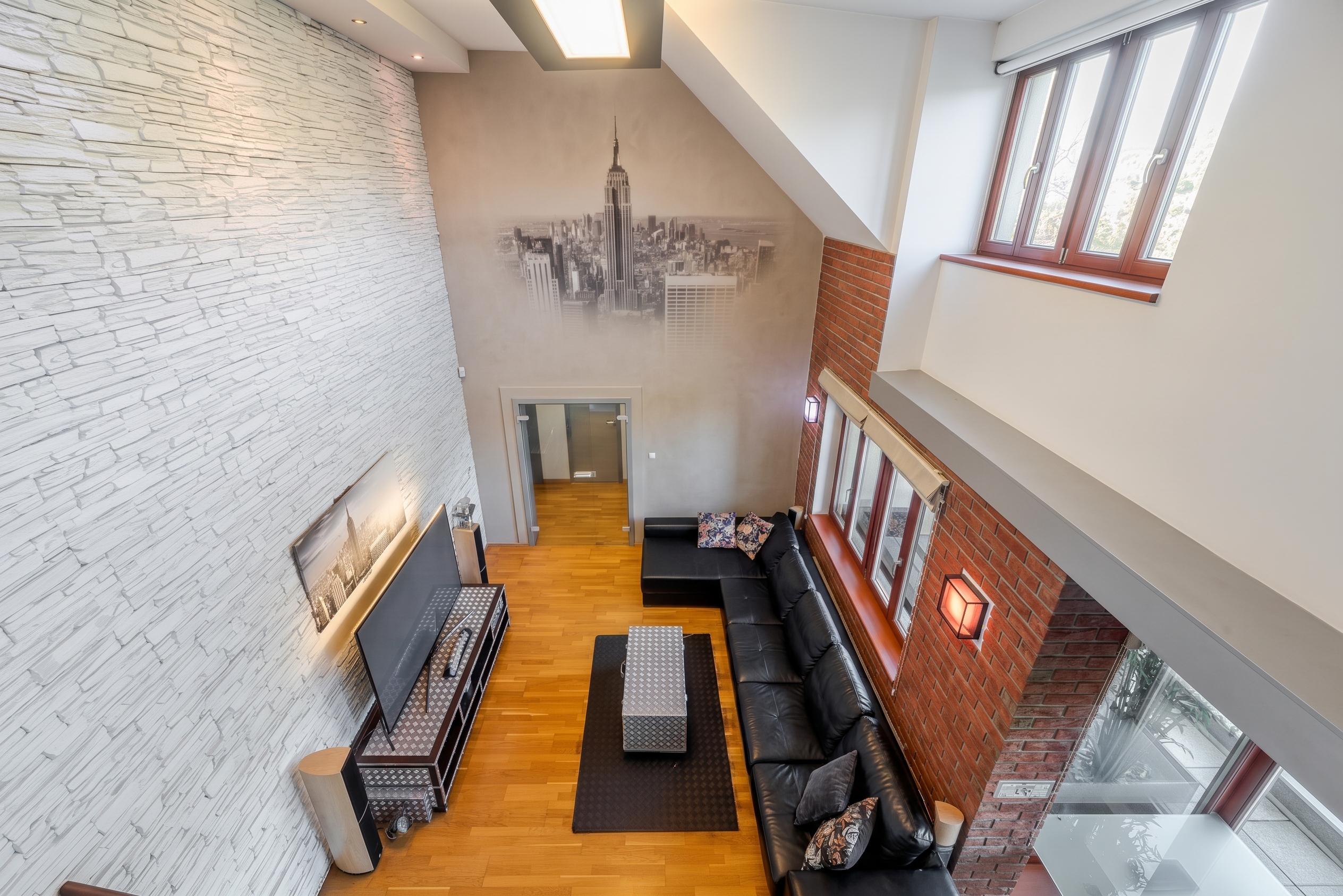 High-angle view of a modern living room with a white stone wall, red brick accents, black leather sofa, and NYC wall mural. [AI-generated text] [Upraveno AI]