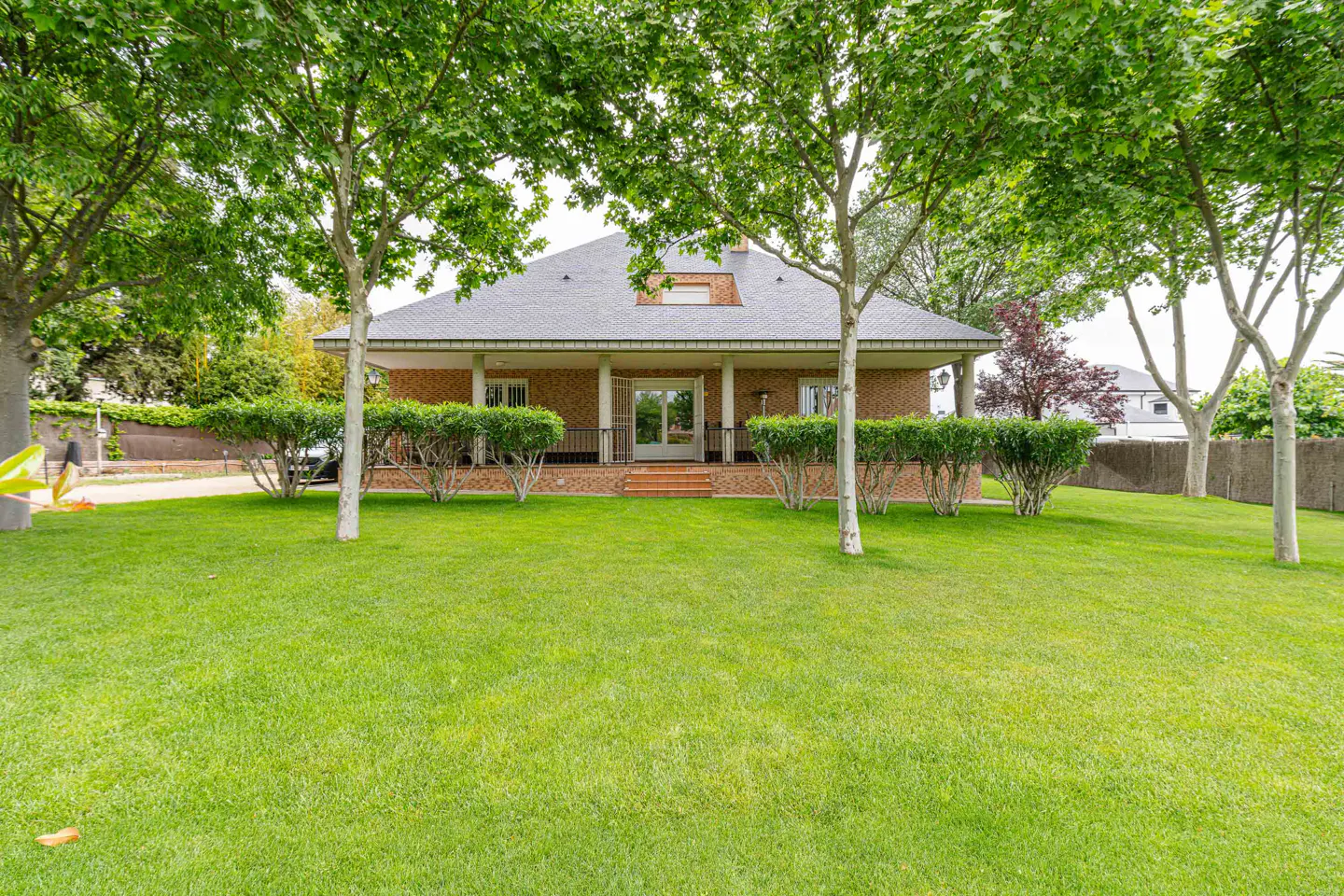 Brick house with a gray roof and white columns, surrounded by green trees and a large lawn.