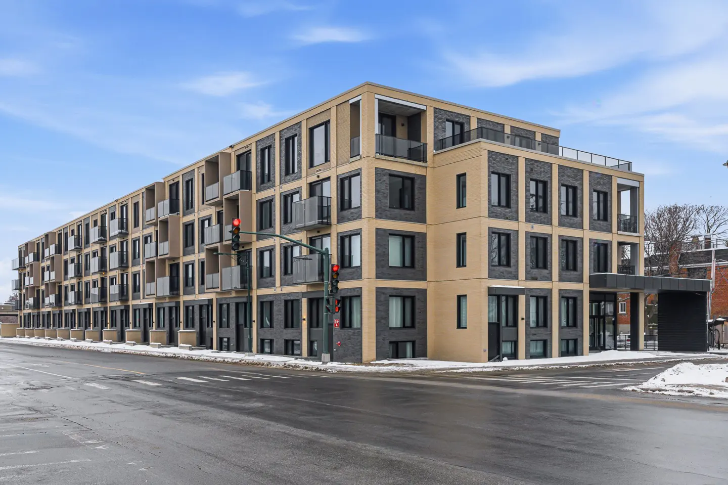 Modern apartment building with balconies, tan and gray brick, on a city street with snow.