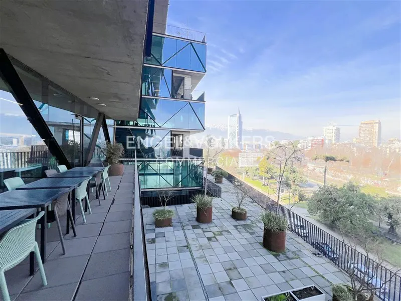 Outdoor patio with tables and chairs, part of a modern building with glass facade, overlooking a city skyline.