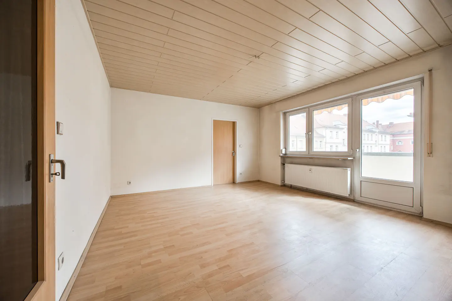 Empty room with light wood flooring, white walls, a wooden ceiling, and a glass door leading to a balcony.