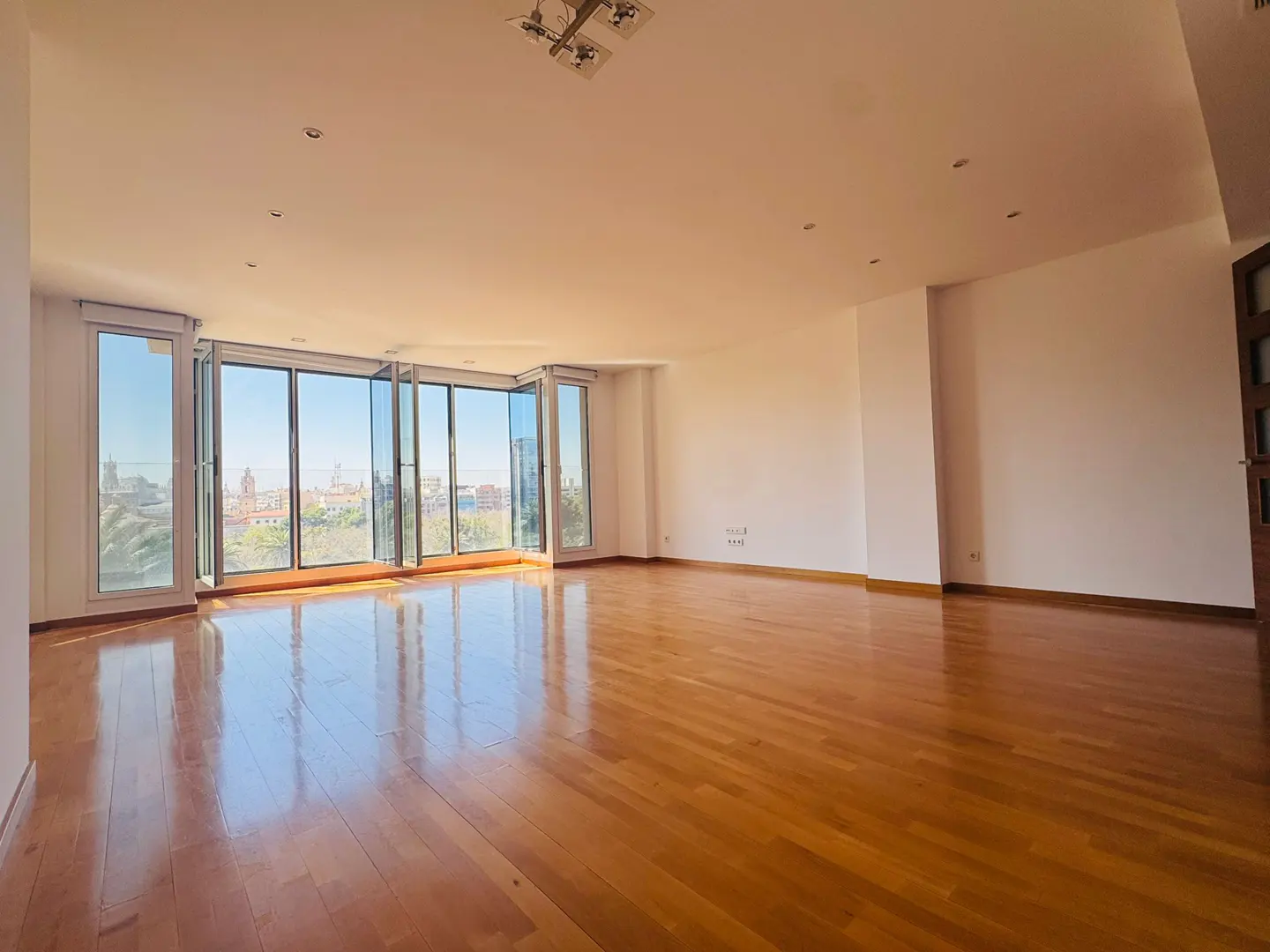Bright, empty room with hardwood floors and white walls. Large windows offer a city view.