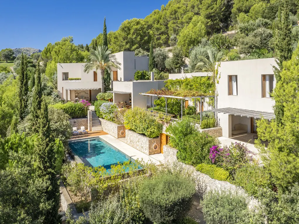 Luxury villa with a pool nestled in lush greenery on a hillside, under a clear blue sky.
