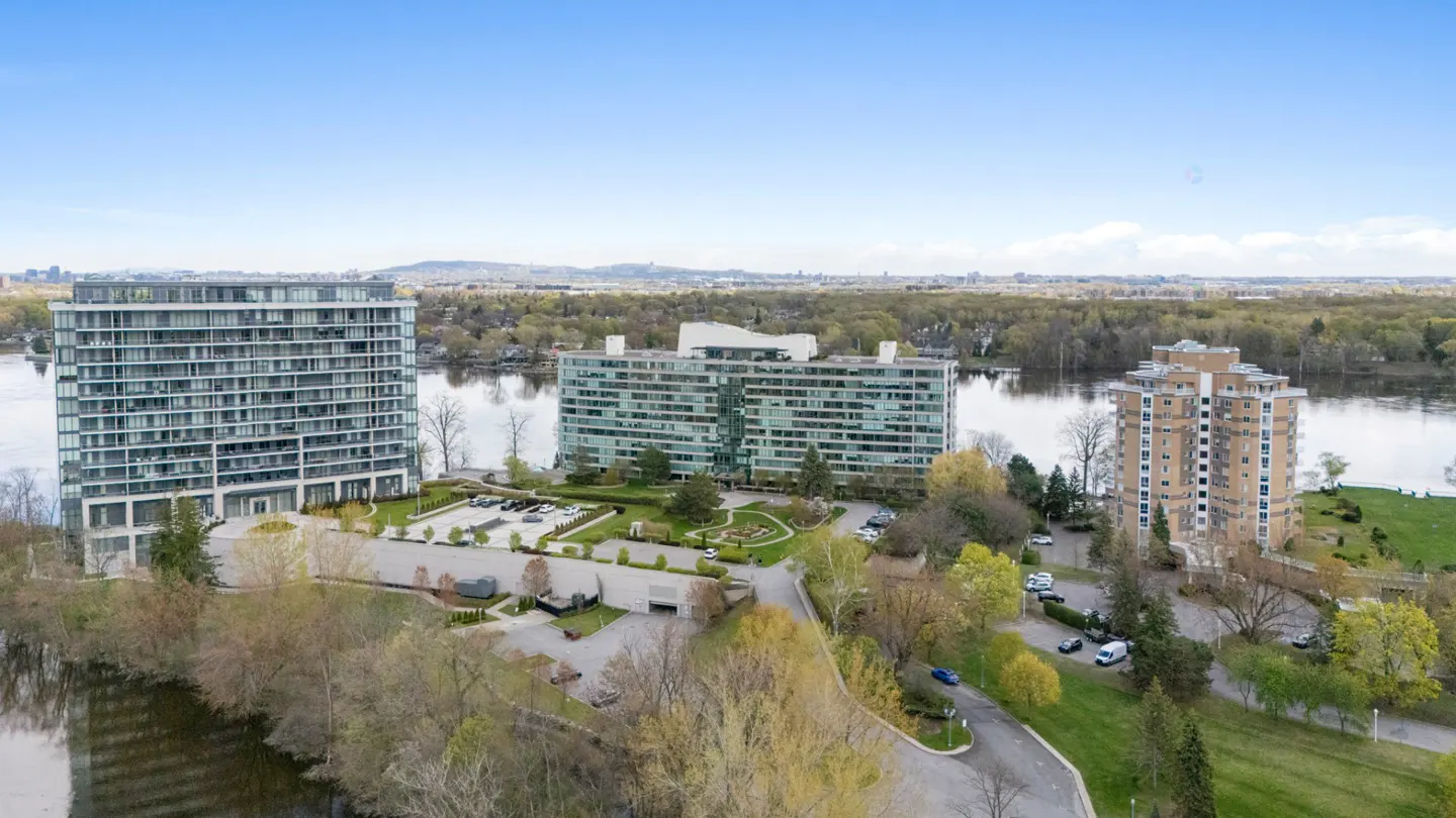 Aerial view of three high-rise apartment buildings on a peninsula surrounded by water and trees under a blue sky.