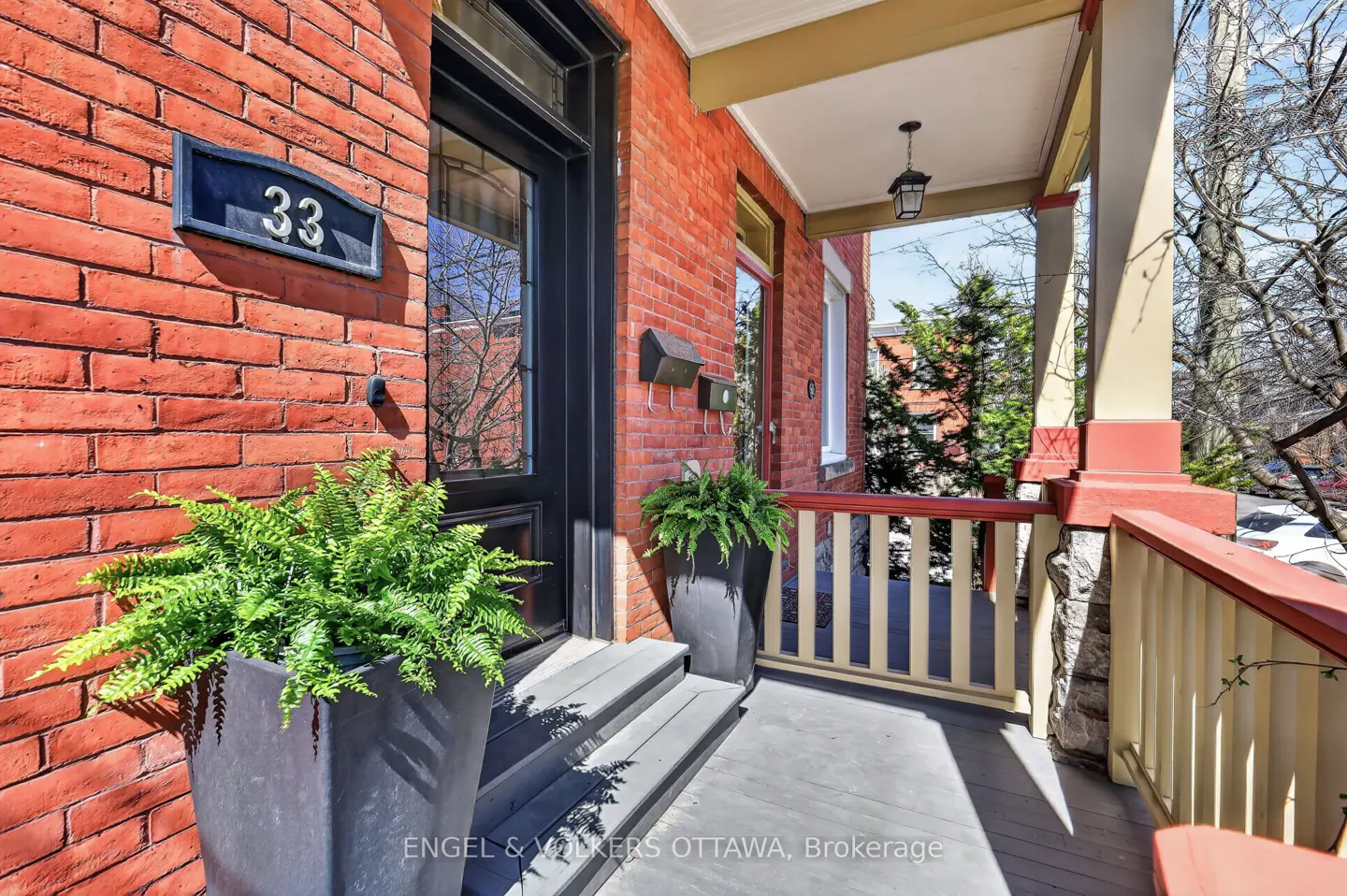 Red brick house at 33 with a black door and porch. Ferns in pots flank the steps.