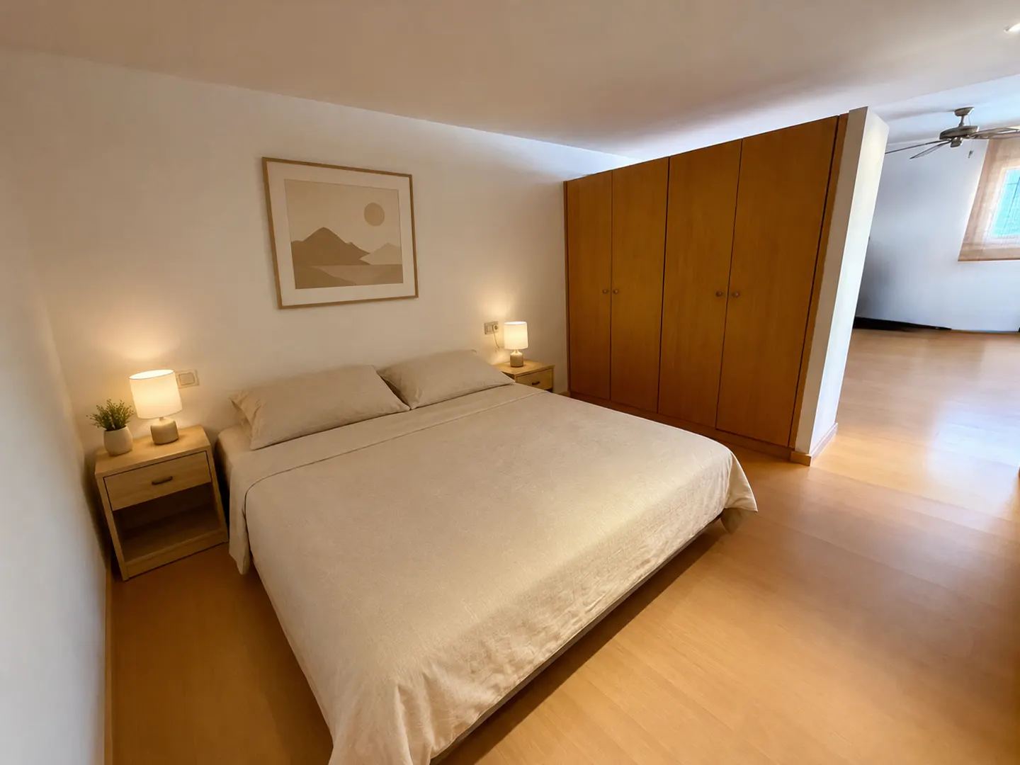 A bedroom with a beige bed, wooden nightstands with lamps, a minimalist wall print, and a large wooden wardrobe.