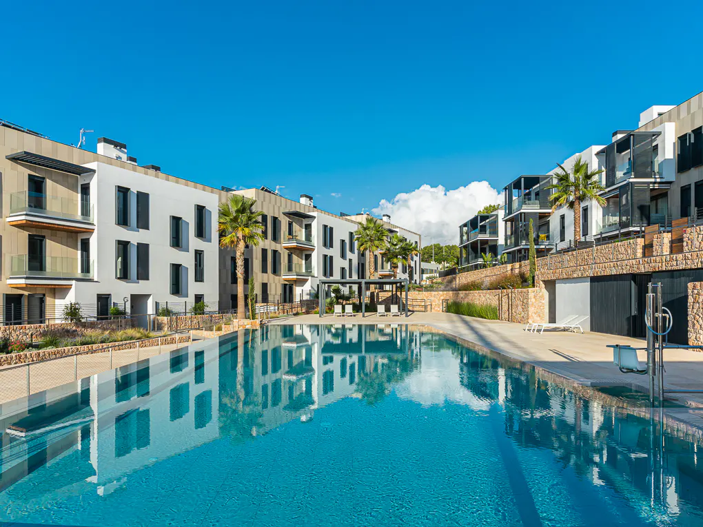 A turquoise pool reflects modern white buildings under a clear blue sky with palm trees.