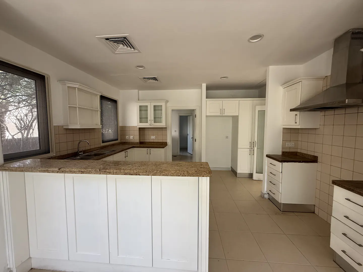 A bright kitchen with white cabinets, granite countertops, and beige tile flooring. A large window provides natural light.