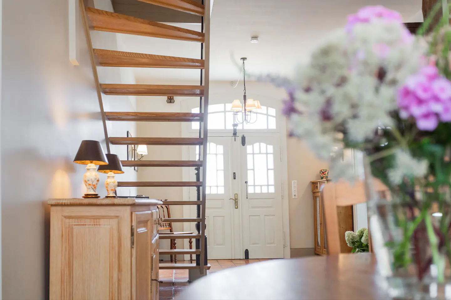 Interior view of a home featuring a wooden staircase, a cabinet with lamps, and a white double door with glass panels.