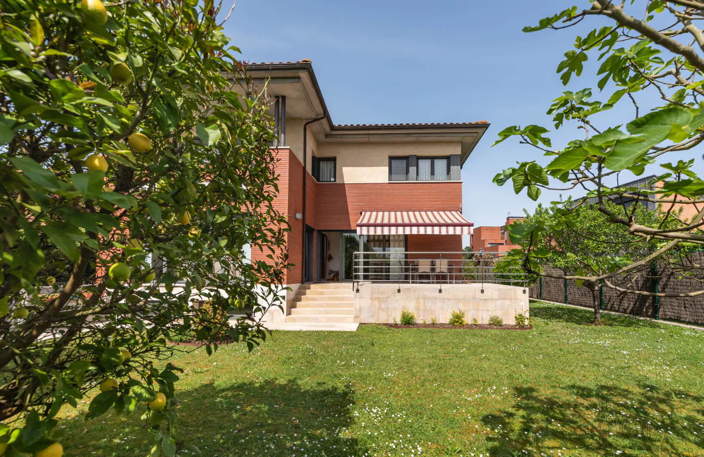 Exterior view of a two-story house with a red brick facade and a green lawn, framed by trees.