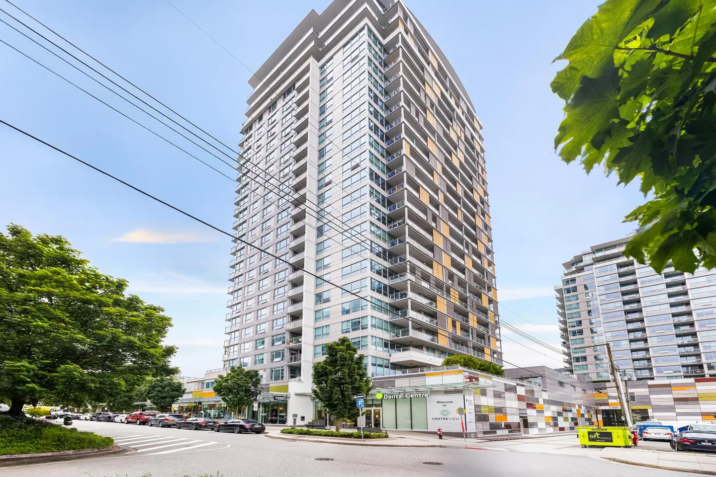 Exterior view of a modern high-rise apartment building with glass windows and balconies, street view with cars and trees.