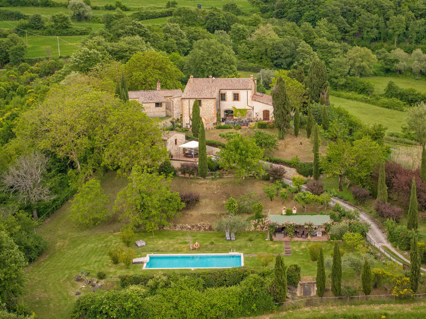 Aerial view of a stone house with a red tile roof, pool, and lush green landscape.