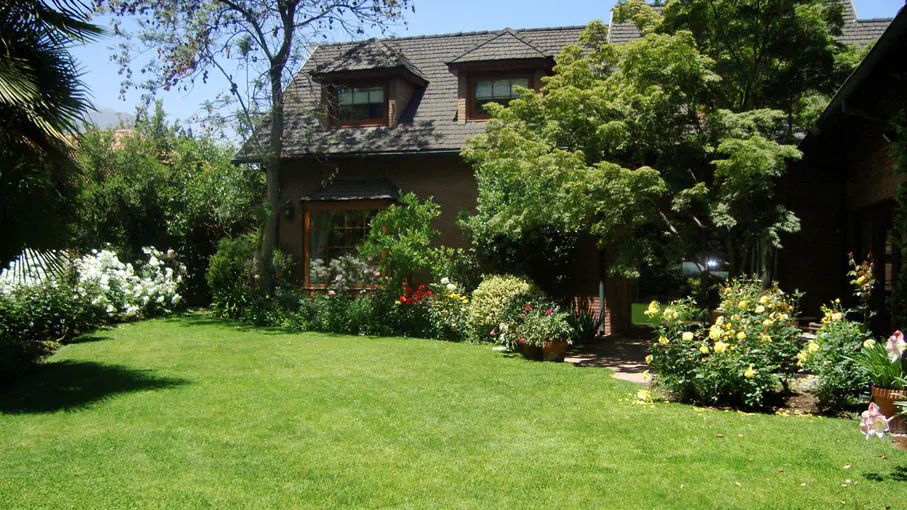 A brown house with a gray roof is surrounded by green trees and a lawn.