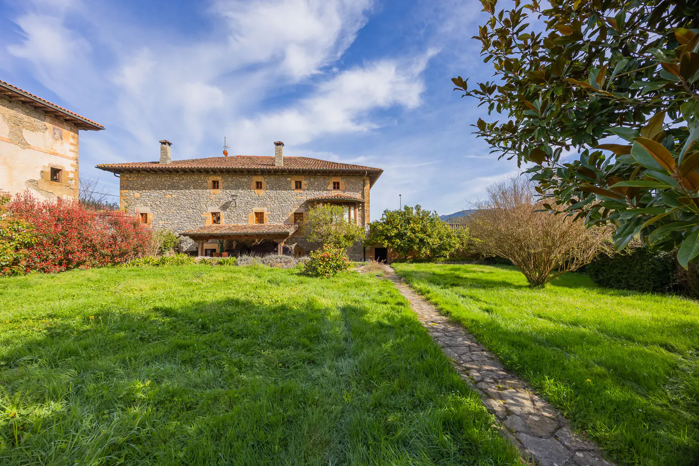 Stone house with a red tile roof and a green lawn under a blue sky with white clouds.