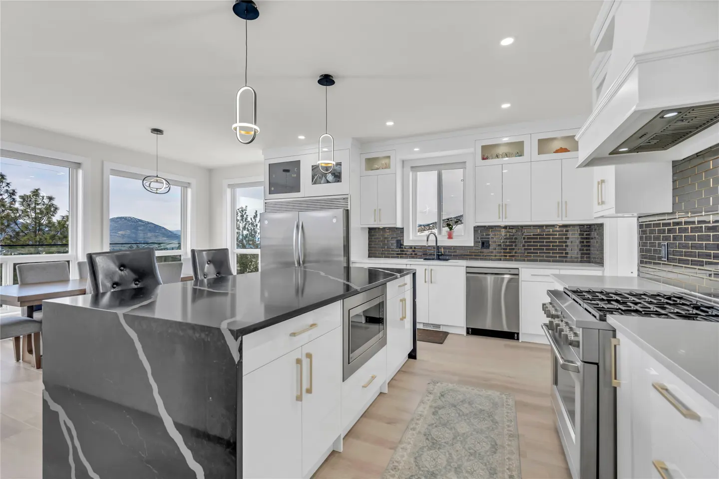 Bright, modern kitchen with white cabinets, stainless steel appliances, and a black marble island. Large windows offer a scenic mountain view.