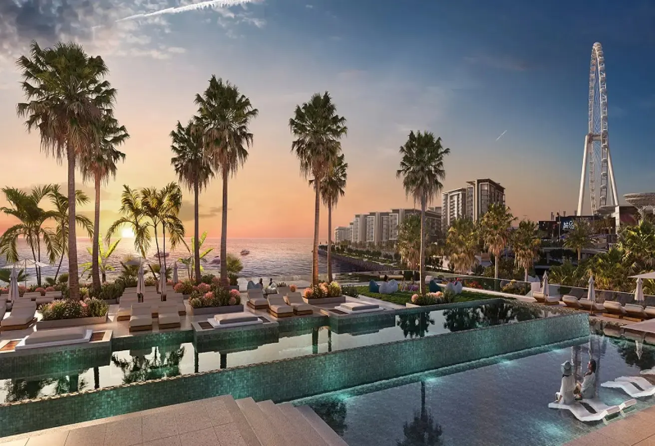 Luxury infinity pool at sunset with palm trees, lounge chairs, modern buildings, and a giant Ferris wheel in the distance.