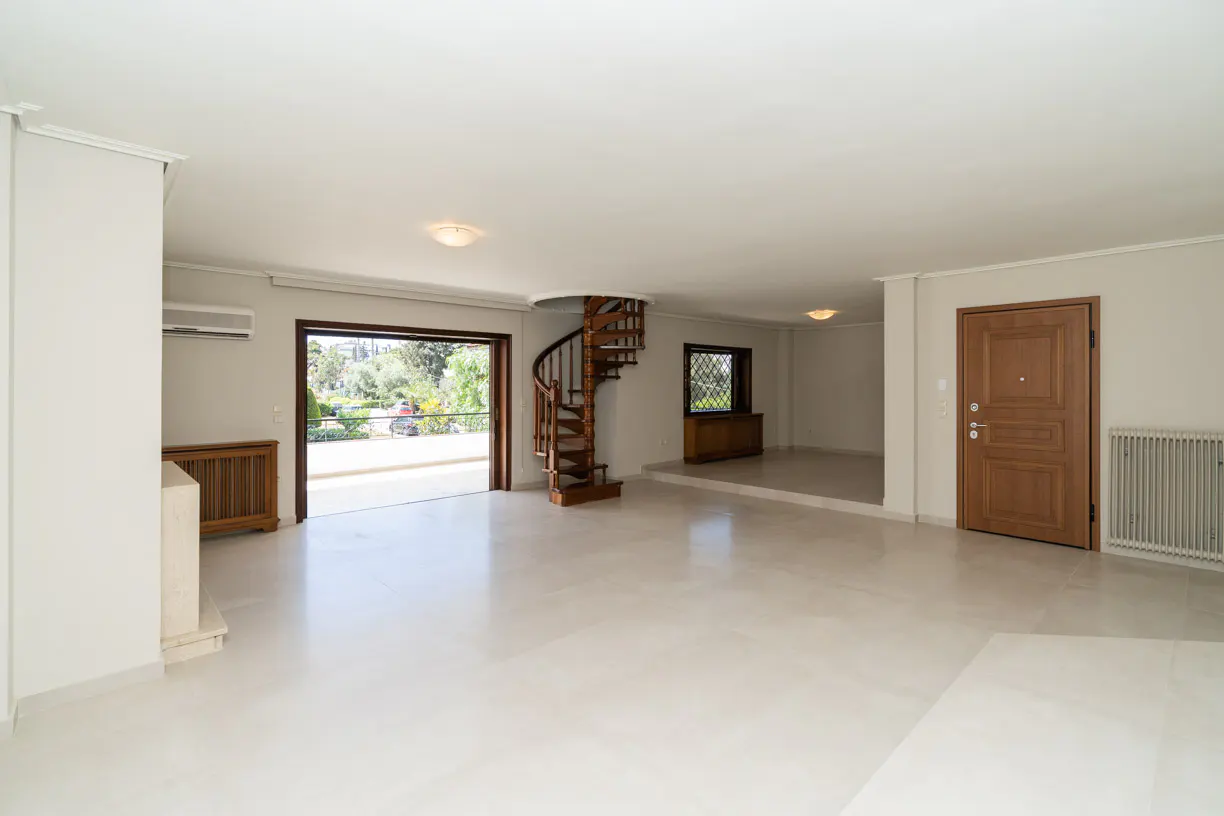 Spacious white living room with a wooden spiral staircase, a large open balcony door, and a wooden entrance door.