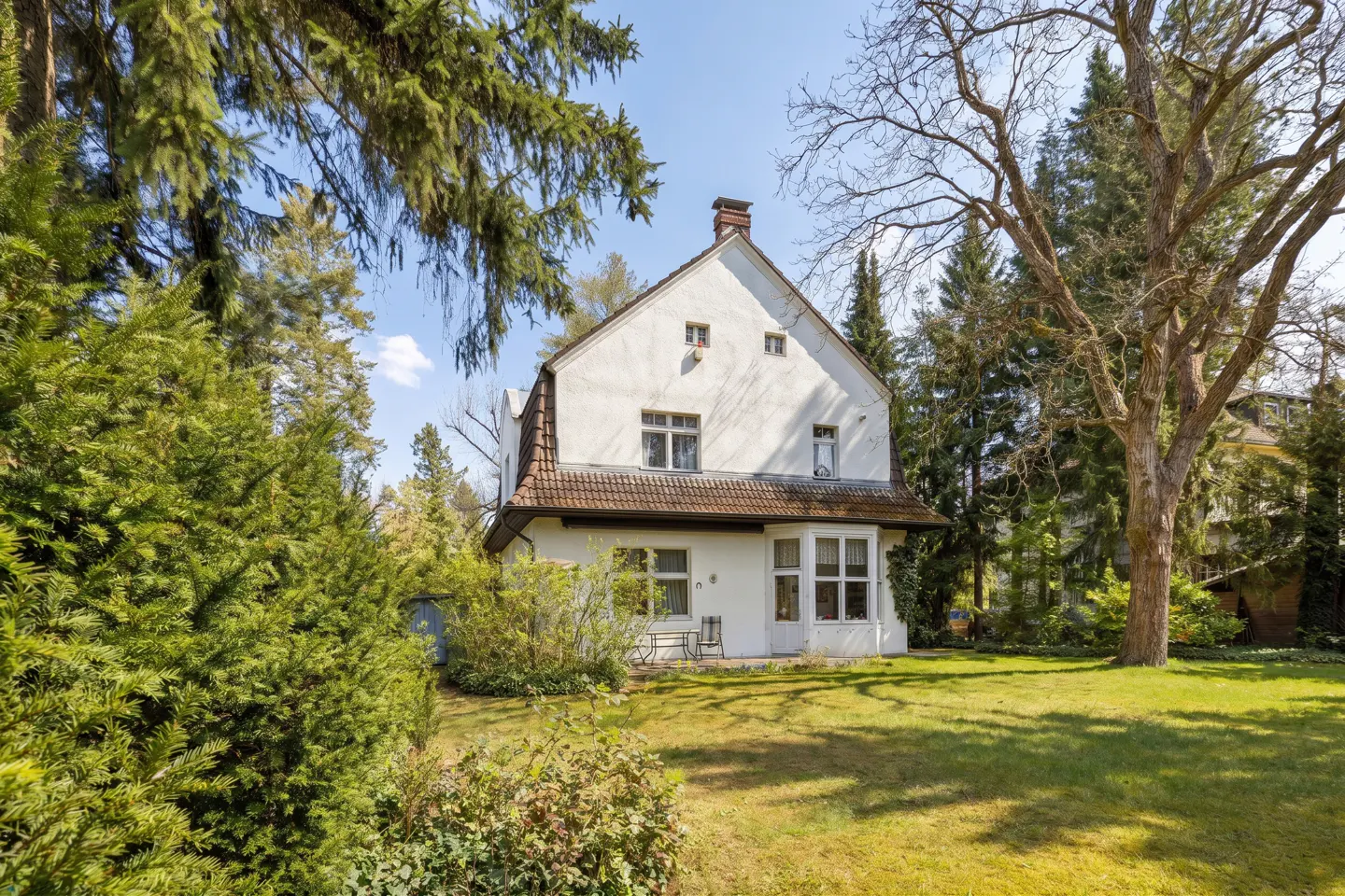 Two-story white house with a red tile roof, surrounded by green trees and a lawn.