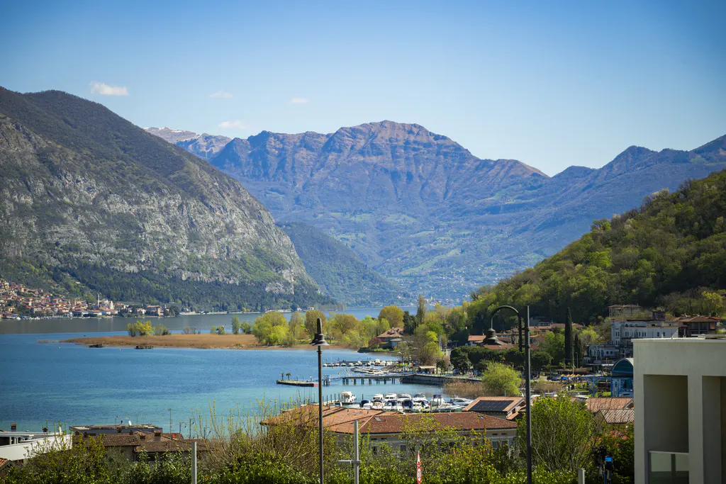 Scenic view of Lake Como, Italy, with mountains, blue water, a marina with boats, and houses with red tile roofs.
