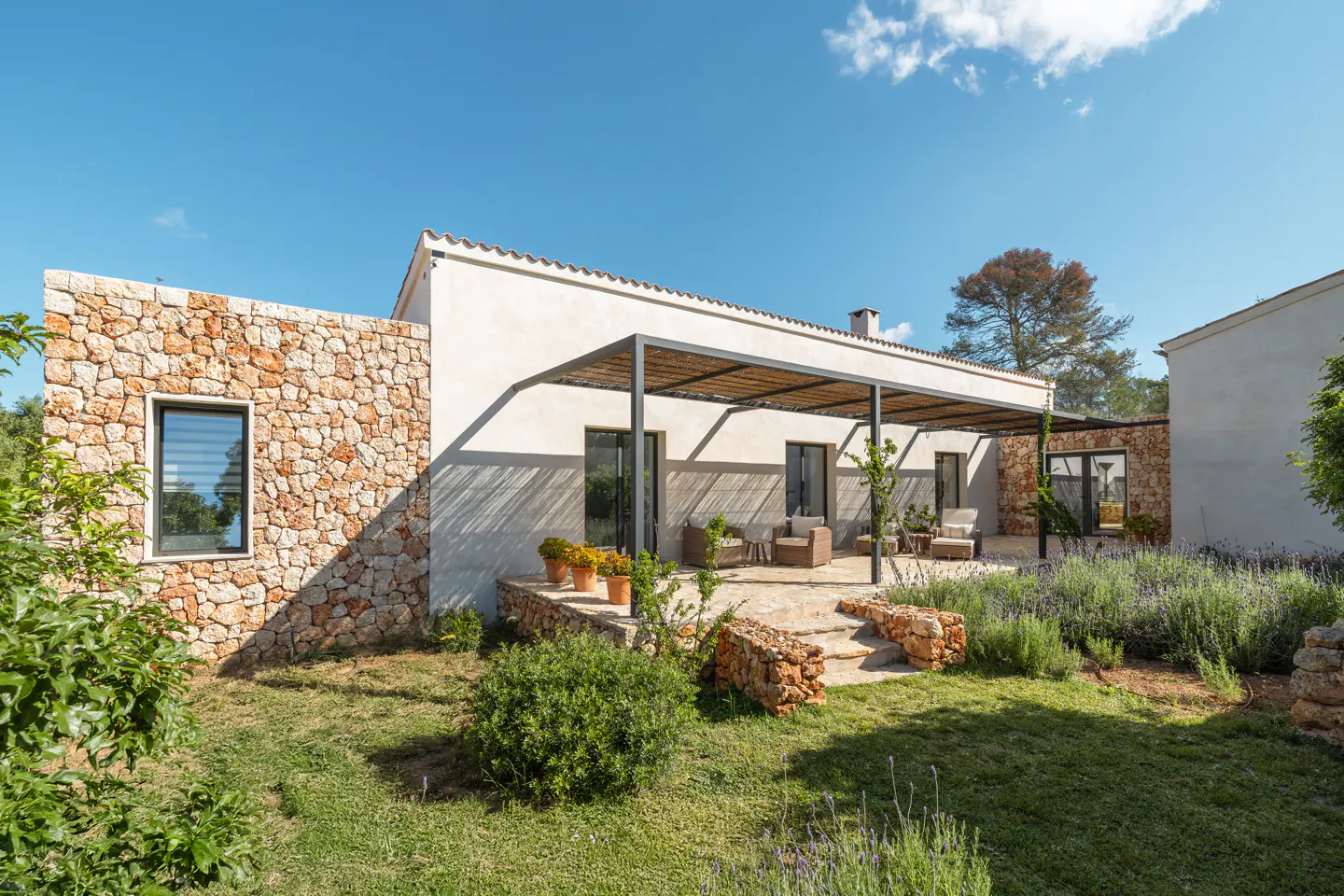Exterior view of a modern stone house with a covered patio and green lawn under a blue sky.