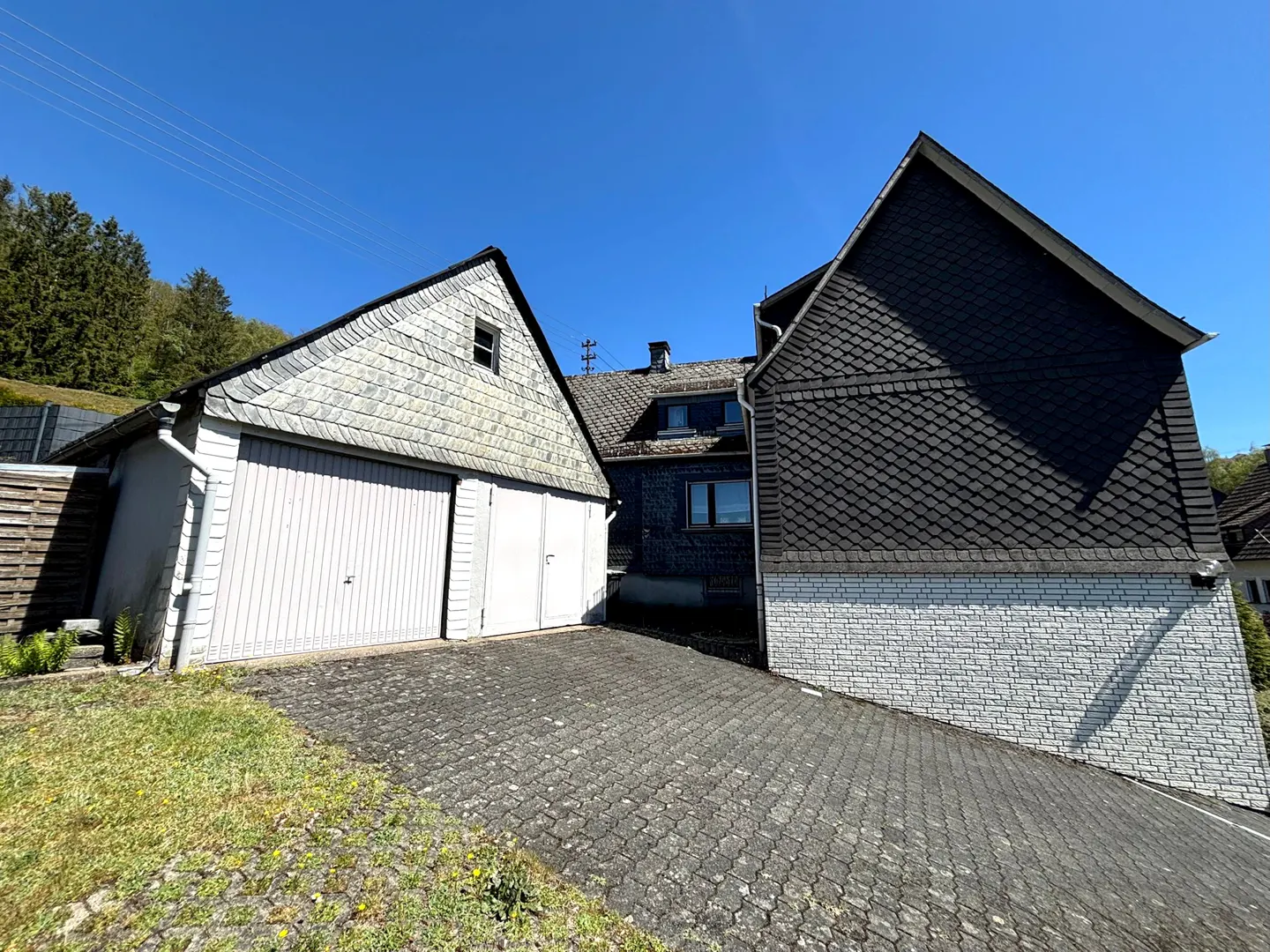 Exterior view of a house with a gray shingled roof and a white garage door on a sunny day.