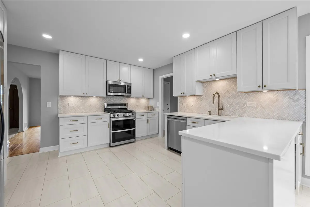 Bright, modern kitchen with white cabinets, stainless steel appliances, and a white countertop island. Herringbone backsplash and light tile flooring.
