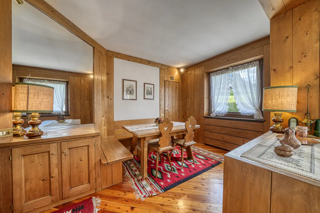 Cozy dining room with wood-paneled walls, a wooden table with heart-shaped chairs, and a red patterned rug.