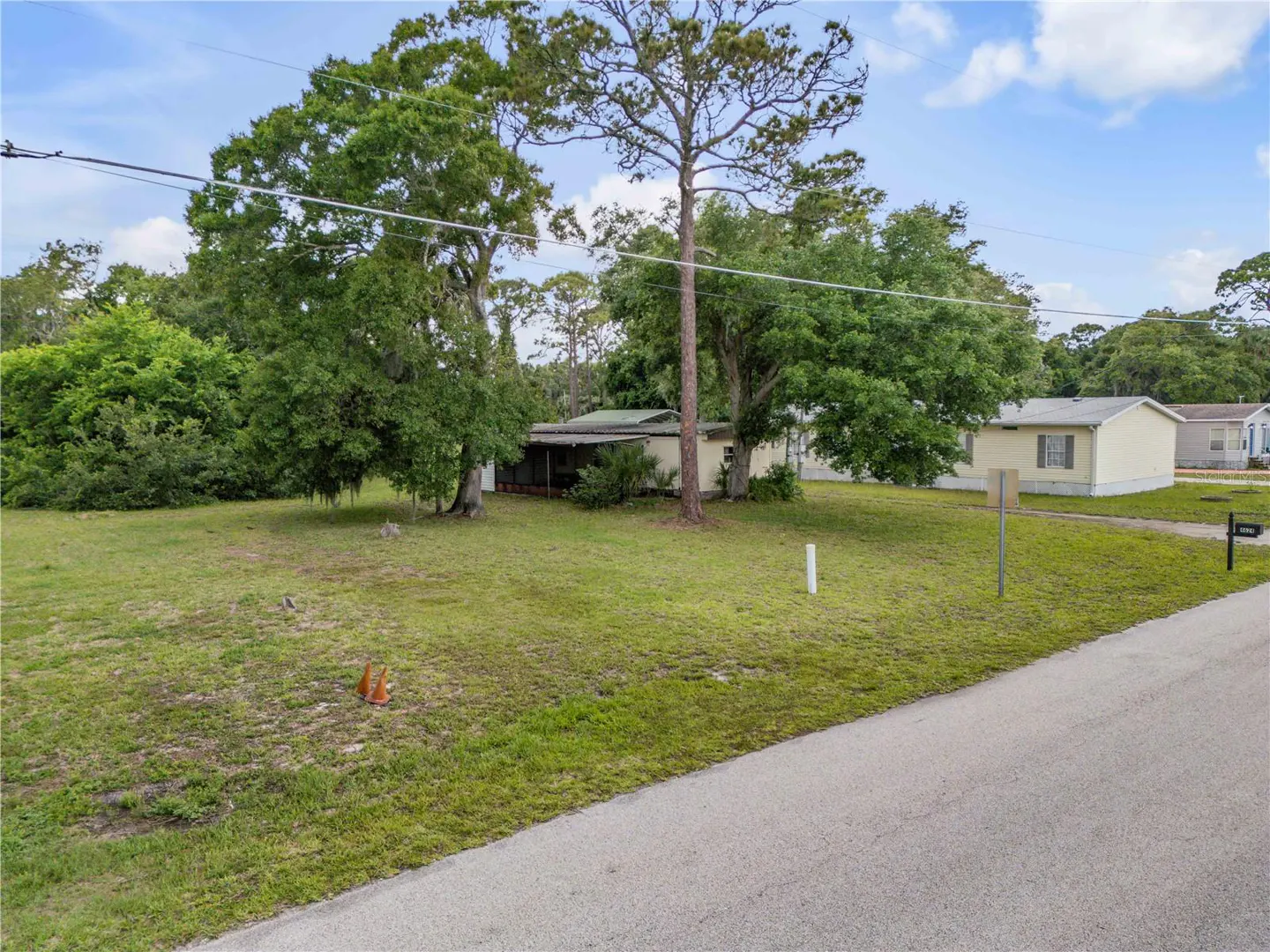 A wide shot of a grassy lot with trees, a small house, and a street in the foreground.