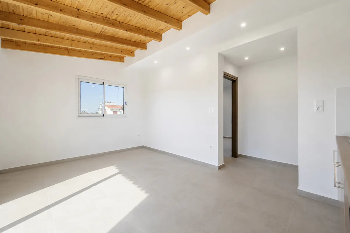 Bright, empty room with white walls, light gray tile floors, and a natural wood beamed ceiling with recessed lighting.