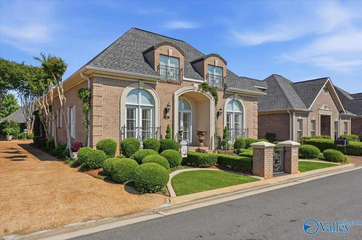Brick house with arched windows, dormers, and manicured landscaping under a blue sky.