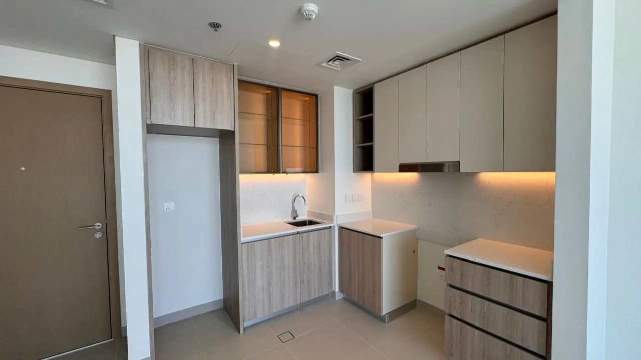 Modern kitchen with light wood cabinets, white countertops, under-cabinet lighting, and a small sink.