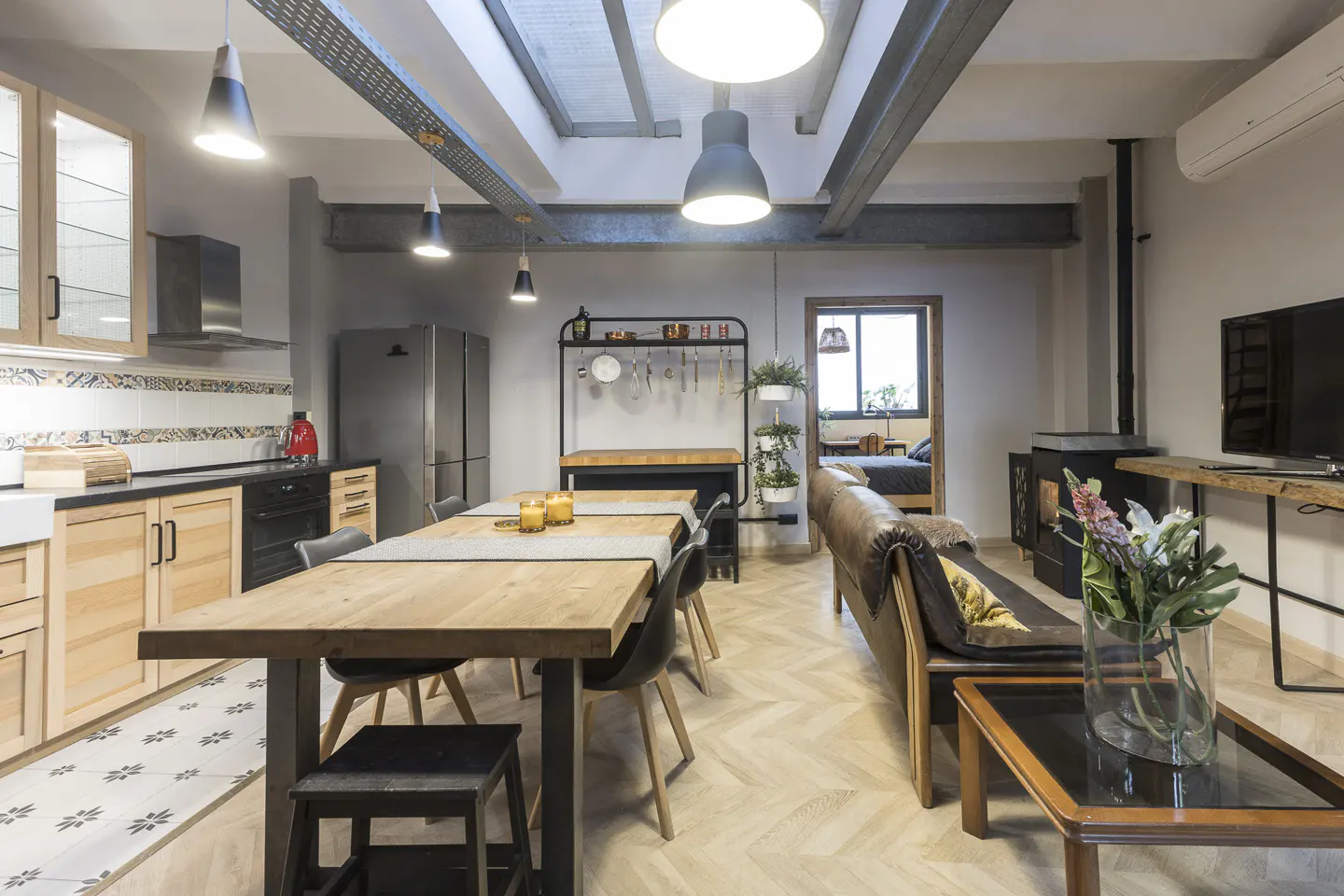 Open-concept living space with kitchen, dining, and living areas. Wood floors, table, and cabinets. Gray walls and metal accents.