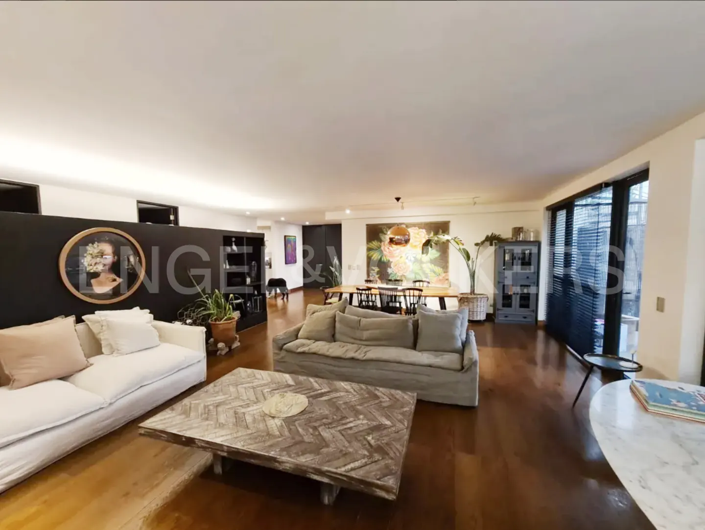 Wide shot of a modern living room with hardwood floors, sofas, a dining table, and large windows.