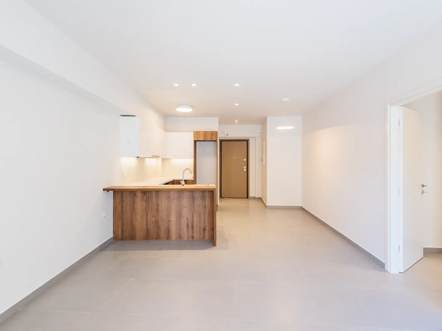 Modern open-plan kitchen with white walls, light tile floors, and a wood-paneled breakfast bar island.